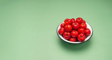 Yeşil arka planda beyaz bir tabakta olgun kırmızı acerola kirazı. Yüksek C vitamini ve antioksidan meyveler. Mesaj için yer var. Yakın plan. Sağlıklı meyve kavramı