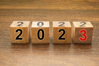 Tahta bir masanın üzerinde 2023 ve 2022 harfleri olan tahta küpleri. Yan görüş. Yeni yıl arifesi ve 2022 'yi 2023' e değiştirmek.