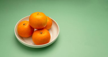 Yeşil arka planda beyaz bir tabakta taze portakalların üst görüntüsü. Sağlıklı meyve kavramı. Yakın plan fotoğraf. Metin için boşluk