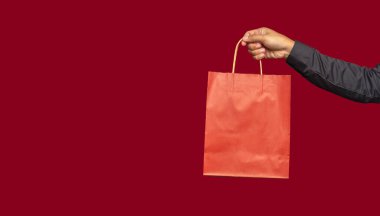 Kırmızı arka planda dururken kırmızı bir kese kağıdının saplı olduğu bir el resmi. Paketleme şablonu modeli. Teslimat hizmeti, alışveriş ve reklam alanı kavramı