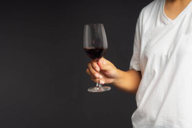 Gri arka planda dururken kırmızı şarap kadehini tutarken yakın plan. Mesaj için yer var. İçecek ve rahatlama kavramı