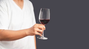 Gri arka planda dururken kırmızı şarap kadehini tutarken yakın plan. Mesaj için yer var. İçecek ve rahatlama kavramı