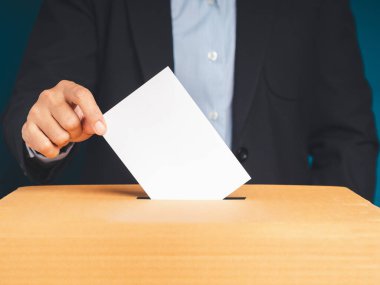 Seçimlerde oy pusulasını mavi arka planlı sandığa koyan elle seçmen. Özgürlük demokrasi kavramı. Yakın plan fotoğraf.