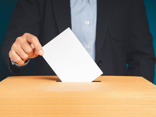 Рука избирателя держит бюллетень положить в урну для голосования на месте выборов с синим фоном. Концепция свободы демократии. Крупный план