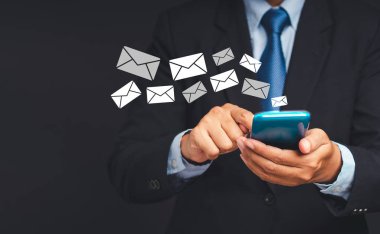 Takım elbiseli bir işadamı gri arka planda dururken e-posta ikonu olan bir akıllı telefon kullanıyor. Mesaj için yer var. İletişim ve teknoloji kavramı