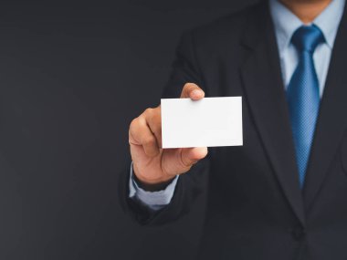 Gri bir arka planda dururken elinde boş bir kartvizit tutan bir el işadamının yakın çekimi. Yakın plan. Mesaj için yer var. İş ve iletişim konsepti