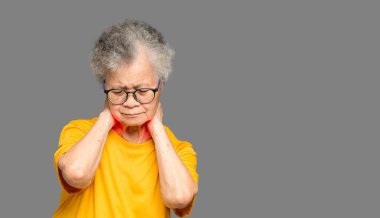 Gri arka planda dururken boynu ağrıyan son sınıf bir kadının portresi. Yaşlılar ve sağlık konsepti