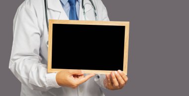 Gri arka planda dururken elinde küçük bir karatahta tutan üniformalı bir doktorun orta kısmı. Mesaj için yer var. Tıbbi personel, tıp ve bilim konsepti. Kaliteli tıbbi hizmetler