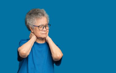 Mavi arka planda dikilirken boynu ağrıyan son sınıf bir kadının portresi. Yaşlılar ve sağlık konsepti