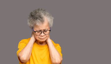 Gri arka planda dururken boynu ağrıyan son sınıf bir kadının portresi. Yaşlılar ve sağlık konsepti