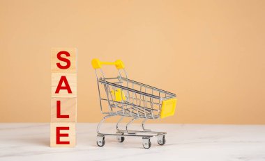 İş alışverişi internet konsepti. Açık turuncu arka planı olan, küçük bir alışveriş arabası ve tahta küplerle dolu mermer bir masa. Metin için boşluk