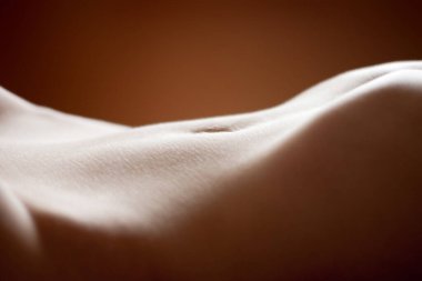 Yumuşak stüdyo ışıklandırmasında kahverengi bir arka planda çıplak bir insanın çıplak bir gövdesinin yakın çekimi.