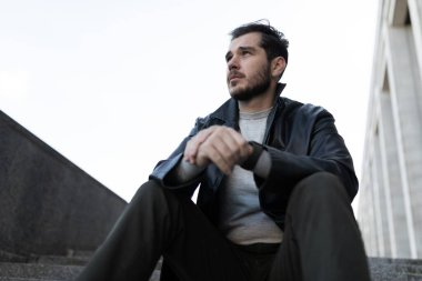 Sokakta yürüyen bir adam depresyon basamaklarında oturur ve yere bakar..