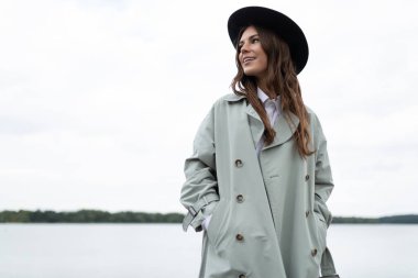 Yağmurluklu ve şapkalı genç bir kadın gezinti güvertesinde yürüyor..