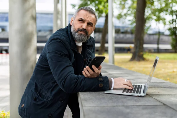 adult bearded man working on laptop outside.