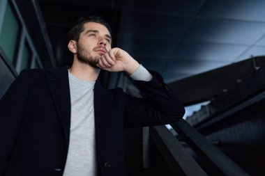 Genç beyaz iş adamı dikiliyor ve düşünceli bir bakışla uzaklara bakıyor..