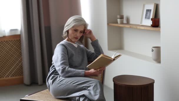 居心地の良い家庭環境の強い女性は静かにソファに座っている本を読みます — ストック動画