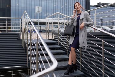 Modern kadın kızıl saçlı komisyoncu bir iş merkezinin girişinde cep telefonuyla konuşuyor..