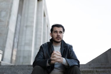 Hüsrana uğramış bunalımlı bir adam dışarıda merdivenlerde otururken uzaya bakıyor..