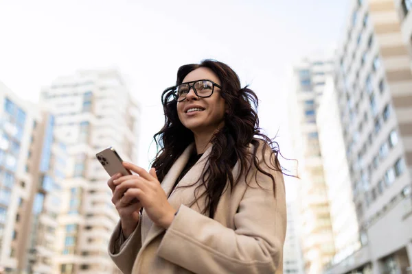 portrait of a female private equity analyst with a phone in her hands and eyeglasses outside.