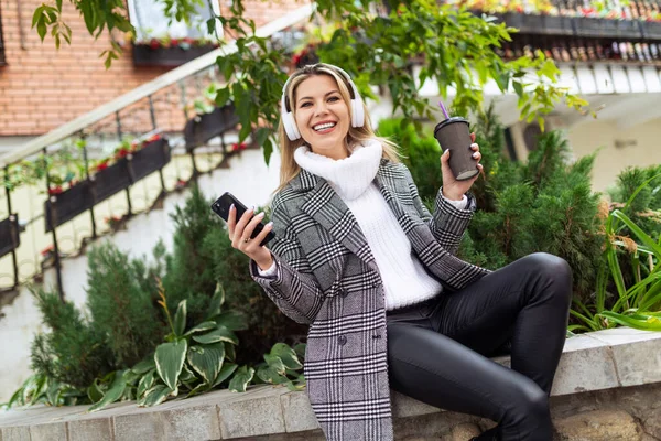 stylish cheerful adult woman in headphones listens to music with pleasure dance with a mobile phone in her hands.