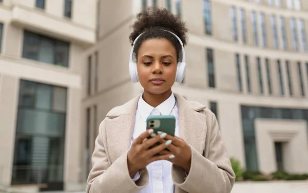 african american stylish woman in headphones on the background of a business center holds a phone in her hands.