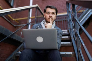 Dışarıda dizüstü bilgisayarı olan düşünceli bir delikanlı oturuyor..