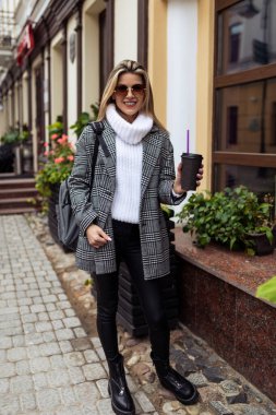 Bir fincan kahveyle şehirde yürüyen bir kadın..