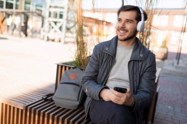 Sırt çantalı genç adam uzaktayken sokakta kulaklıkla müzik dinliyor..