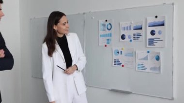 Kadın ofis çalışanı bir sunumda iş konularını iş arkadaşlarıyla konuşurken manyetik panoda bir grafiğe işaret ediyor..
