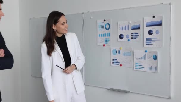 プレゼンテーション中の女性オフィスの従業員は 会議で同僚とのビジネス上の問題を議論しながら 磁気ボード上のグラフを指します — ストック動画