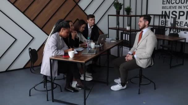 インタビューの男性がオフィスのテーブルに座っている求職者との彼の経験について話します — ストック動画