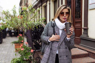 Güzel bir caddenin arka planında bir fincan kahveyle bir kadın turist..