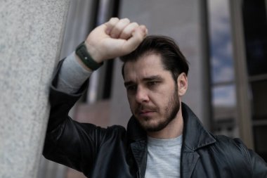 Depresyondaki sakallı adam dışarıda duvara yaslanıyor..