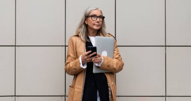 Ellerinde bej bir duvarın arkasında dizüstü bilgisayarı olan olgun yaşlı bir kadın kafası..