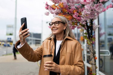Dışarıdaki dükkanın girişinde telefonla konuşan yaşlı bir kadın..