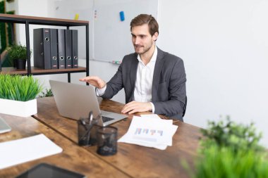 Ofiste evraklar ve belgelerle birlikte bir dizüstü bilgisayarın önünde oturmuş online seminer düzenleyen bir işadamı..