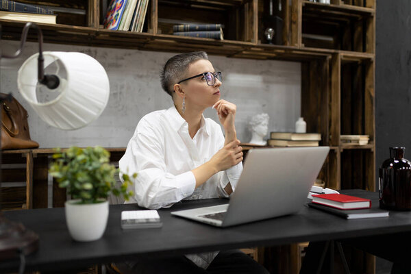 mature business woman at the workplace sitting in glasses thinking in front of an open laptop.