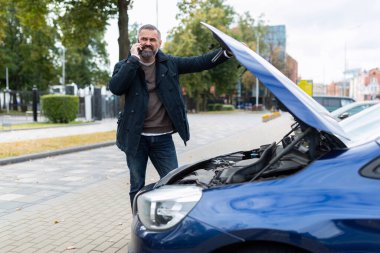Adamın biri telefonda bozuk bir arabanın yanında konuşuyor..