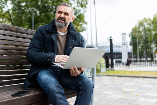 Gray-haired mature man with laptop outside.