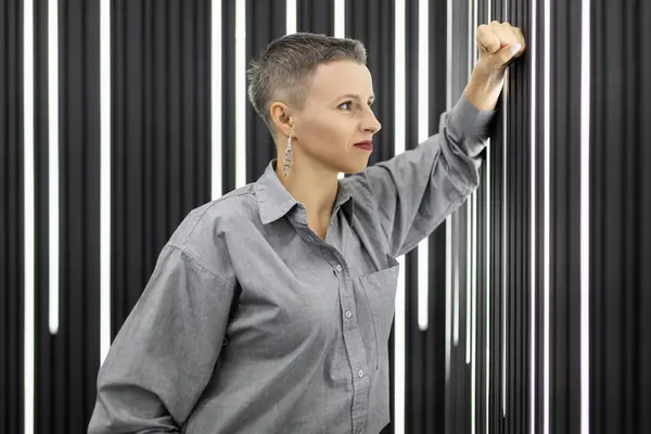portrait of a pensive woman with a short haircut against a black wall.