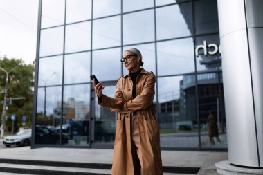 Başarılı yetişkin beyaz kadın iş merkezinin girişindeki telefona bakıyor..