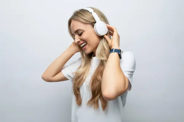 romantic woman sings along to music from headphones among white background.