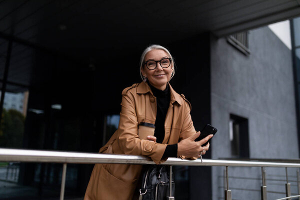 Взрослая белая женщина-бухгалтер с седыми волосами, стоящая на ступеньках бизнес-центра.