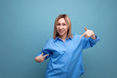 Şanslı sarışın genç milenyum gündelik gömlekli elleri mavi arkaplanda fotokopi alanı olan elbiseleri gösteriyor..