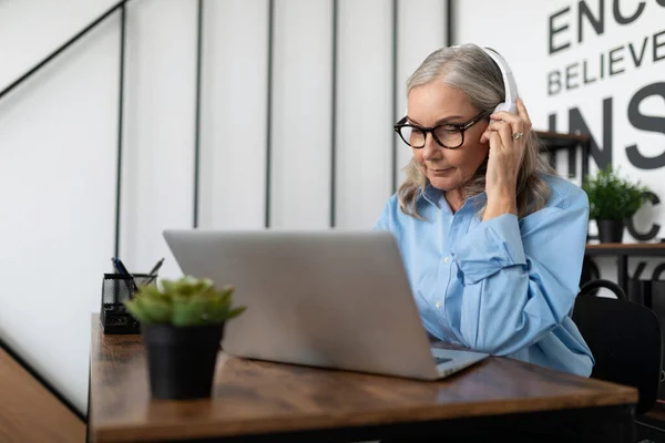 mature adult boss woman with gray hair has a conversation using internet and headset.