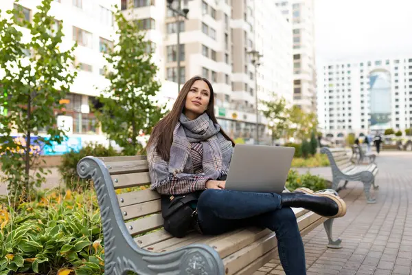 young blond woman journalist with laptop sits on a bench in the city.