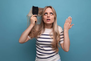 Üzgün, sarışın, saçları dökülen, mavi arka planda saçını tarayan genç bir kadın..