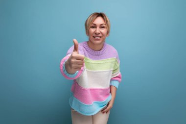 Çizgili kazaklı hoş sarışın kadın mavi arka planda süper bir jest sergiliyor..