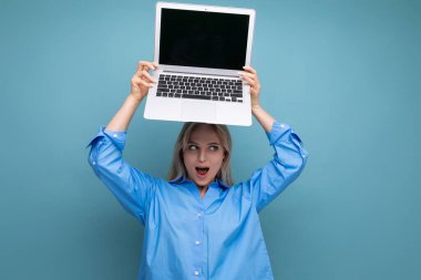 Mavi arka planda web sitesi için boş alanı olan açık dizüstü bilgisayarı olan sarışın bir kızın şok olmuş fotoğrafı..
